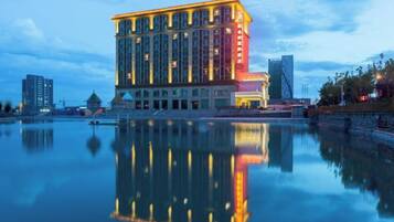A multi-story hotel with a reflection in the water, featuring a prominent entrance and a modern architectural design.