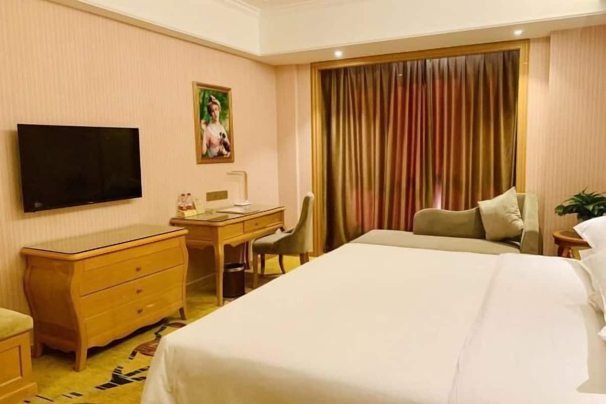 Une chambre d’hôtel avec un lit, un bureau, une chaise, une télévision et un rideau.