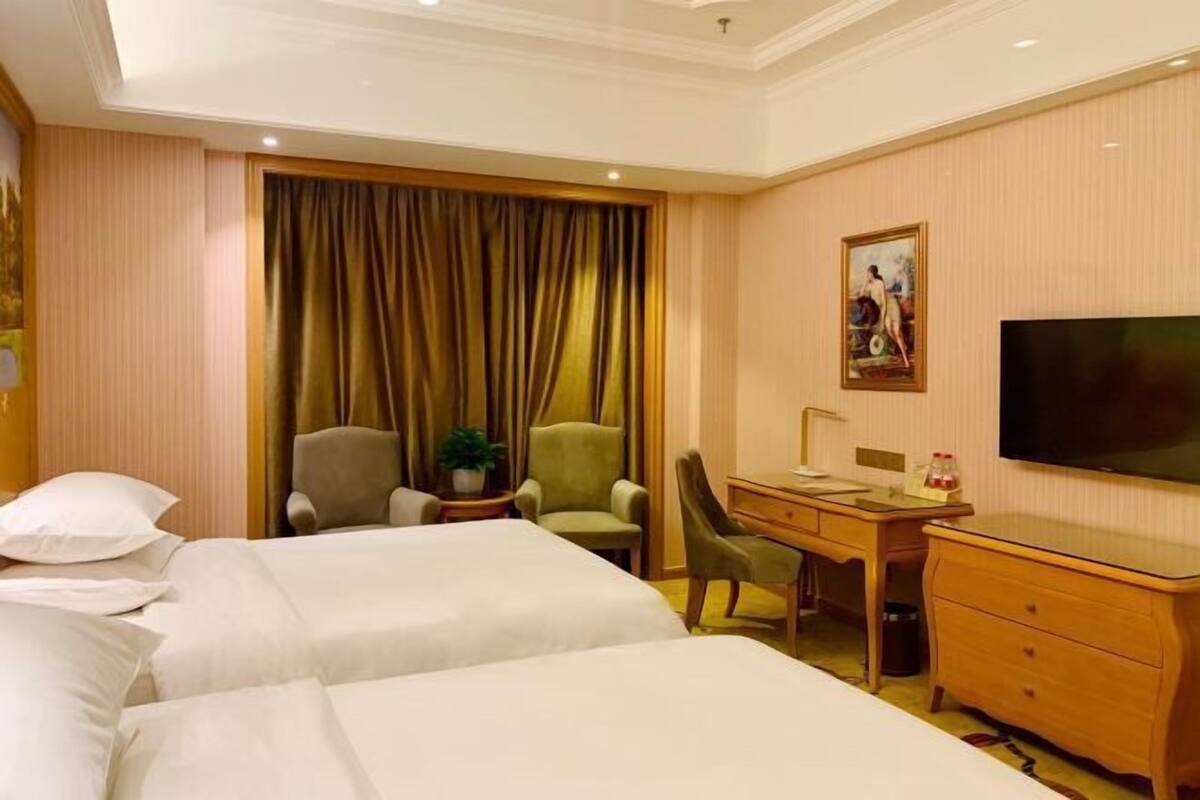 Une chambre d’hôtel avec deux lits, un bureau, une chaise, un téléviseur et un tableau au mur.
