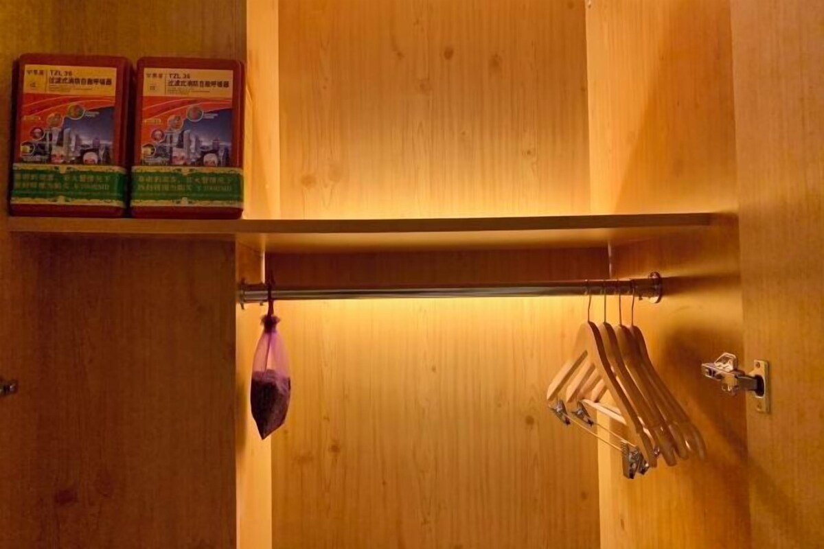 Ein Holzkleiderschrank mit Kleiderstange, ein violettes Kleidungsstück und zwei Kisten auf der obersten Ablagefläche.