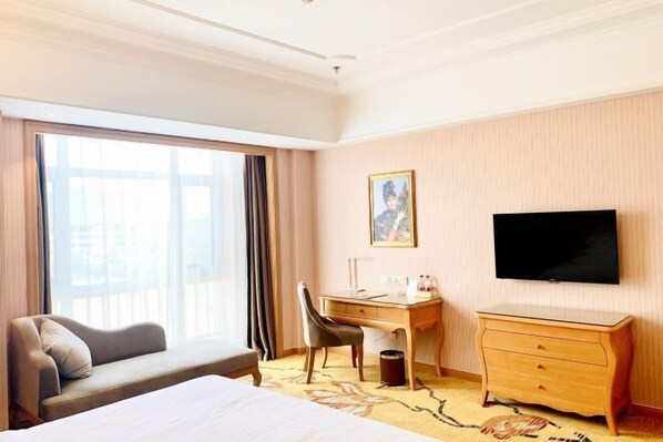 Ein Hotelzimmer mit Bett, Schreibtisch, Stuhl, Fernseher und einem Fenster mit Vorhängen.