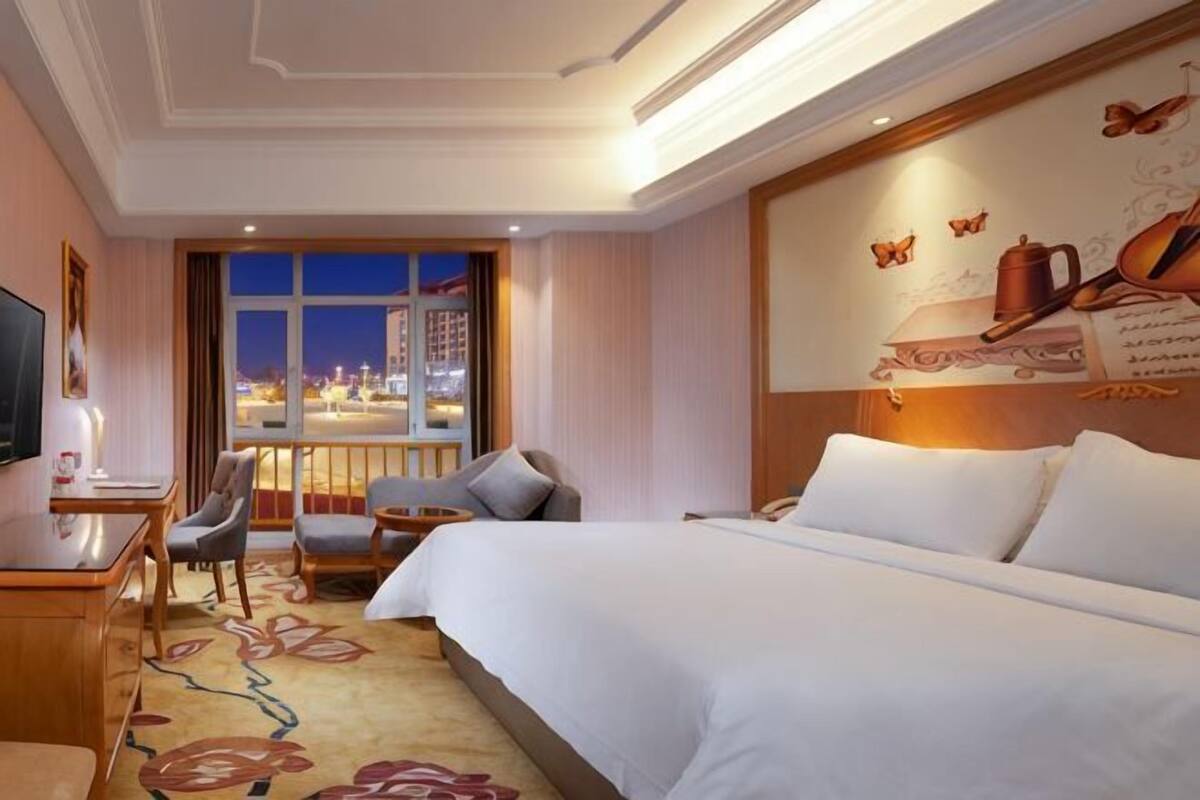 Une chambre d’hôtel avec un grand lit, un bureau avec une chaise, une télévision et une vue sur le paysage urbain par une fenêtre.