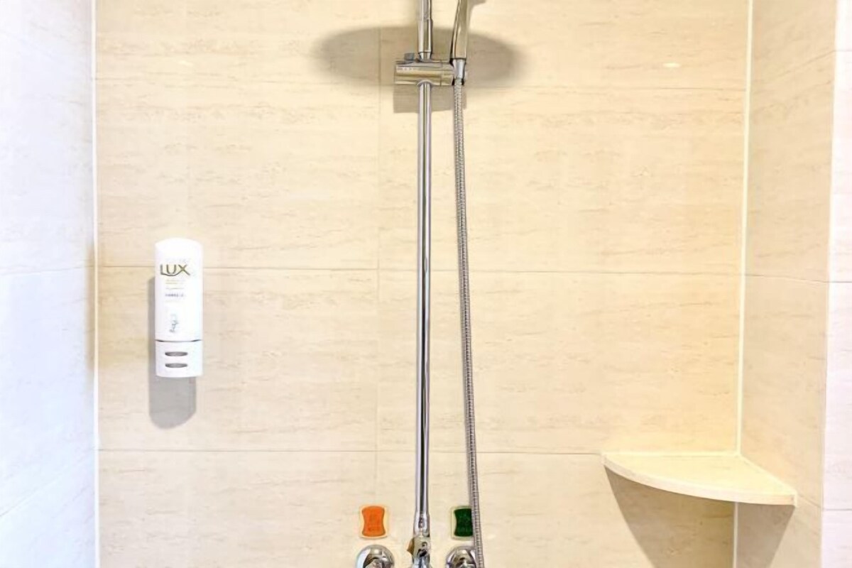 Eine Dusche mit Duschkopf und zwei Handbrausen, einem Seifenspender und einer kleinen Ablagefläche.