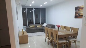 A modern living room with a dining area, a sofa, and a large window with a city view. - Heart of Jerusalem 4 rooms - modern - WIFI (Jerusalem)