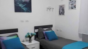 A modern bedroom with two beds, a nightstand, and artwork on the walls. - Heart of Jerusalem 4 rooms - modern - WIFI (Jerusalem)