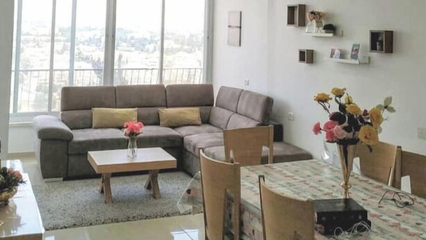 A modern living room with a sectional sofa, a dining table with chairs, and a large window offering a view. - Heart of Jerusalem 4 rooms - modern - WIFI (Jerusalem)