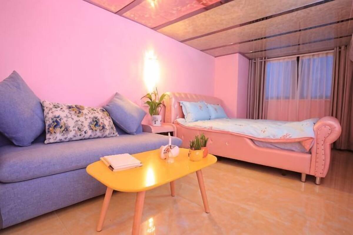 A room with a sofa, a bed, a small table, and a nightstand with a lamp.
