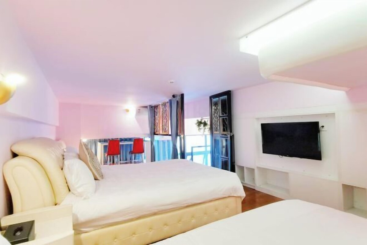 Ein Hotelzimmer mit einem großen Bett, einem an der Wand befestigten Fernseher und einem Balkon mit roten Stühlen.