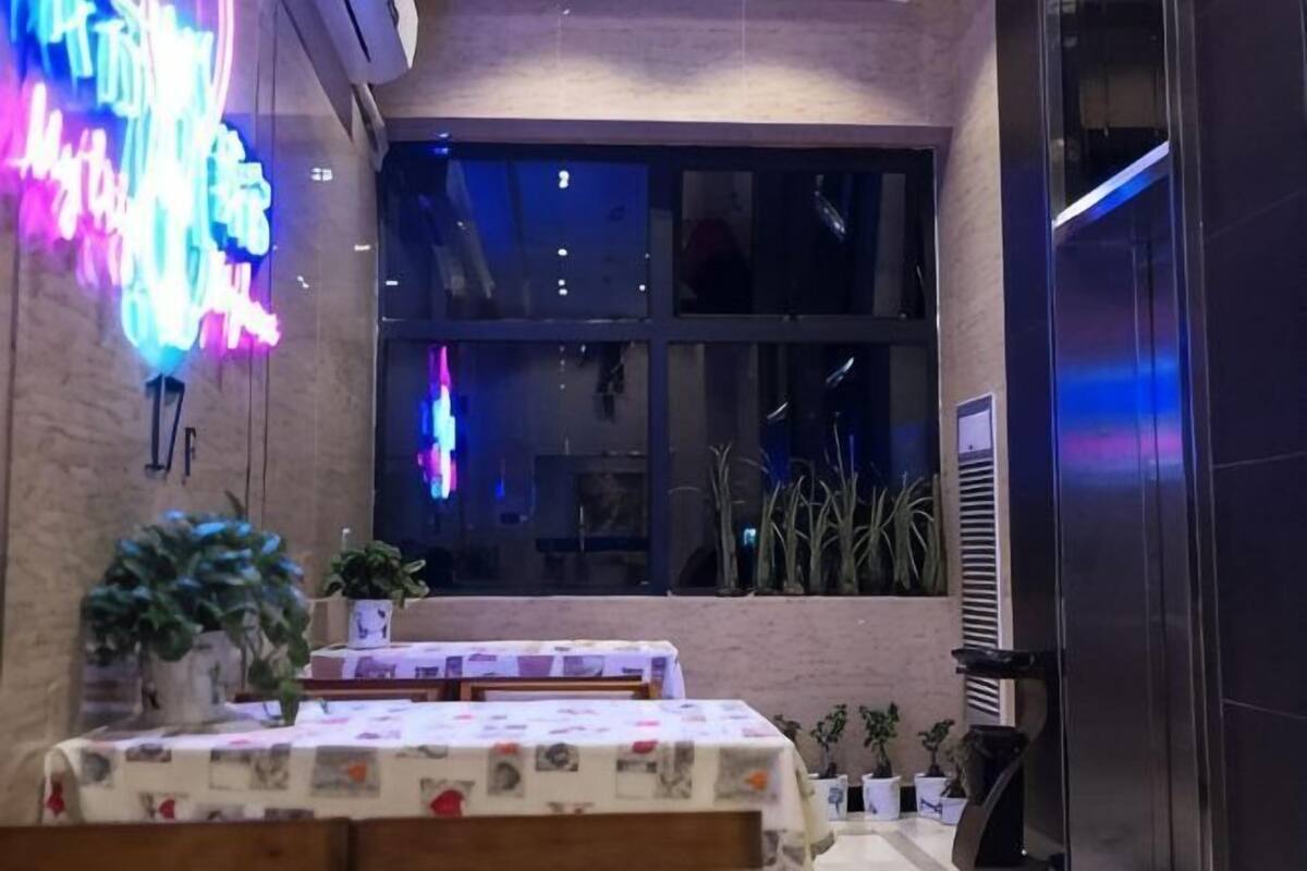 A restaurant with tables, chairs, potted plants, and a neon sign.