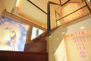 A staircase with wooden steps and a glass railing, leading to a room with a large poster and a wall with hanging pink decorations. - Jiangmen Woxingwosu Apartment (Jiangmen)