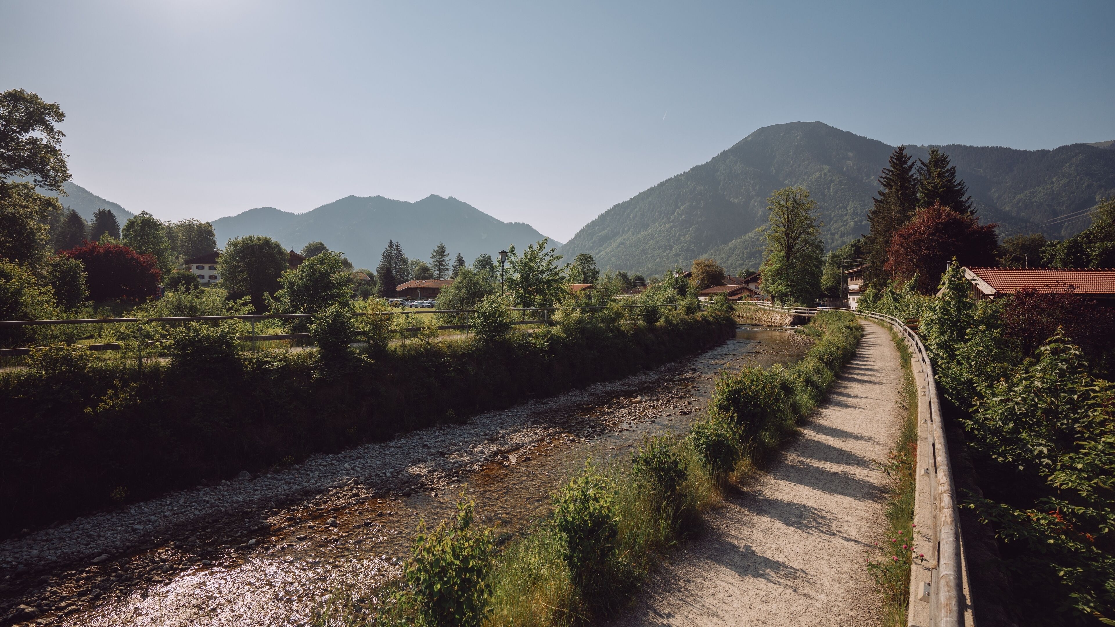 A rural landscape with a river, a dirt path, and houses in the background.