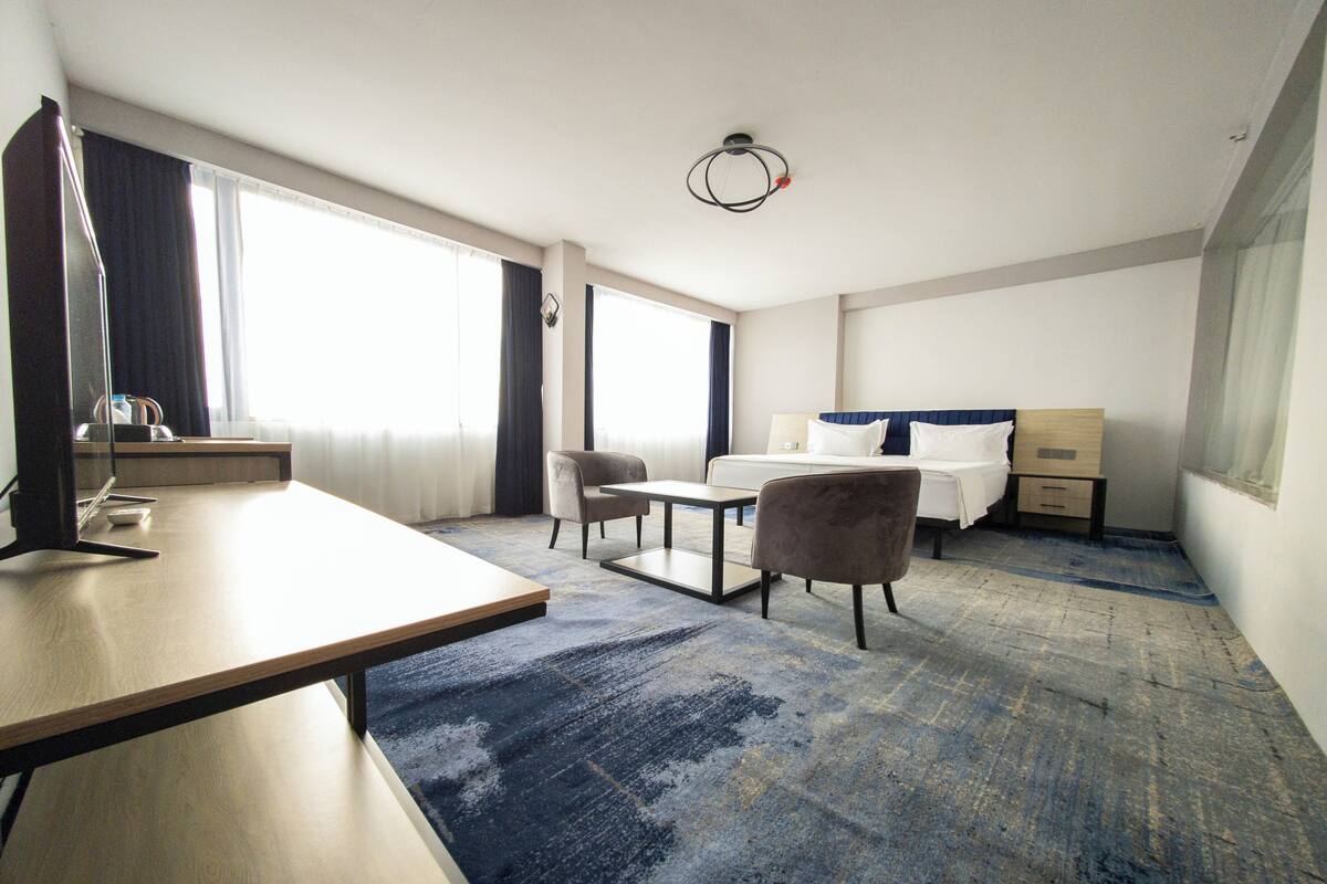 Habitación de hotel con cama, escritorio, silla, televisor y una ventana grande.