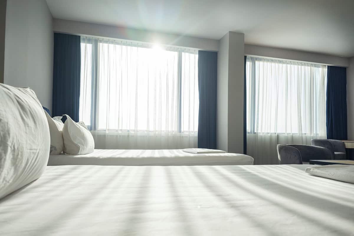 Habitación de hotel con una cama grande, dos ventanas con cortinas, un escritorio y una silla.