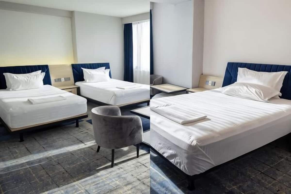 Habitación de hotel con tres camas, un sillón gris y un escritorio.
