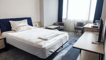 Quarto de hotel com uma cama grande, uma escrivaninha, duas cadeiras e uma televisão.