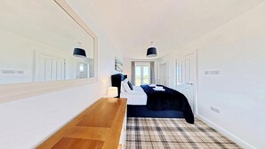 A hotel room with a bed, a wooden table, a mirror, and a view of the outdoors. - Seaview Coastal Cottage - Sleeping 6 in 3 Bedrooms - Pool and Beach Access (Filey)