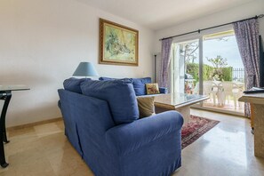 A living room with a sofa, a table, and a painting on the wall. - Apartment with communal pool (Mijas)