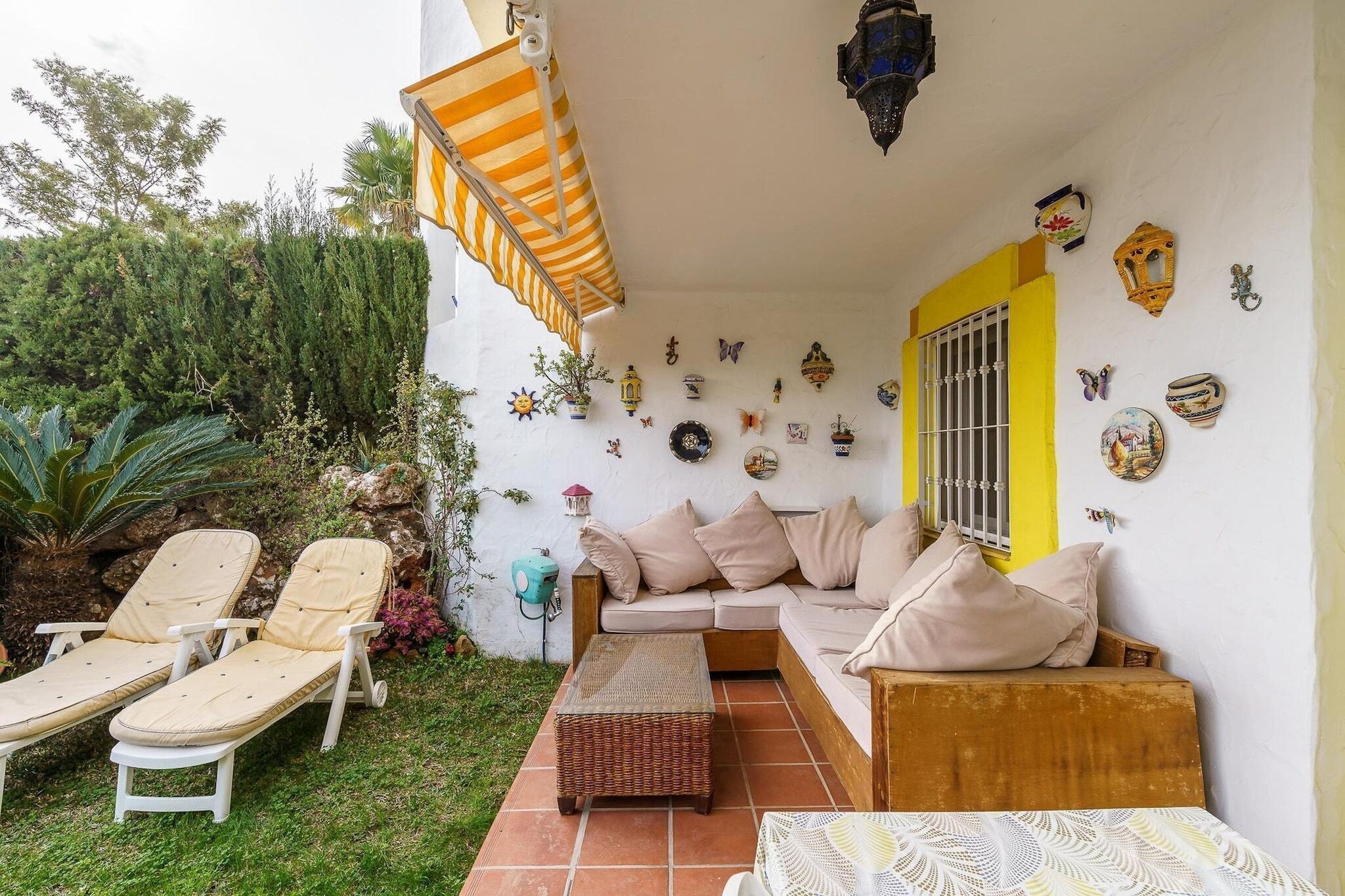 A patio with a sofa, two lounge chairs, a small table, and a decorative wall with various items.