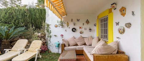 Un patio con un sofá, dos sillones, una mesita y una pared decorativa con varios objetos.