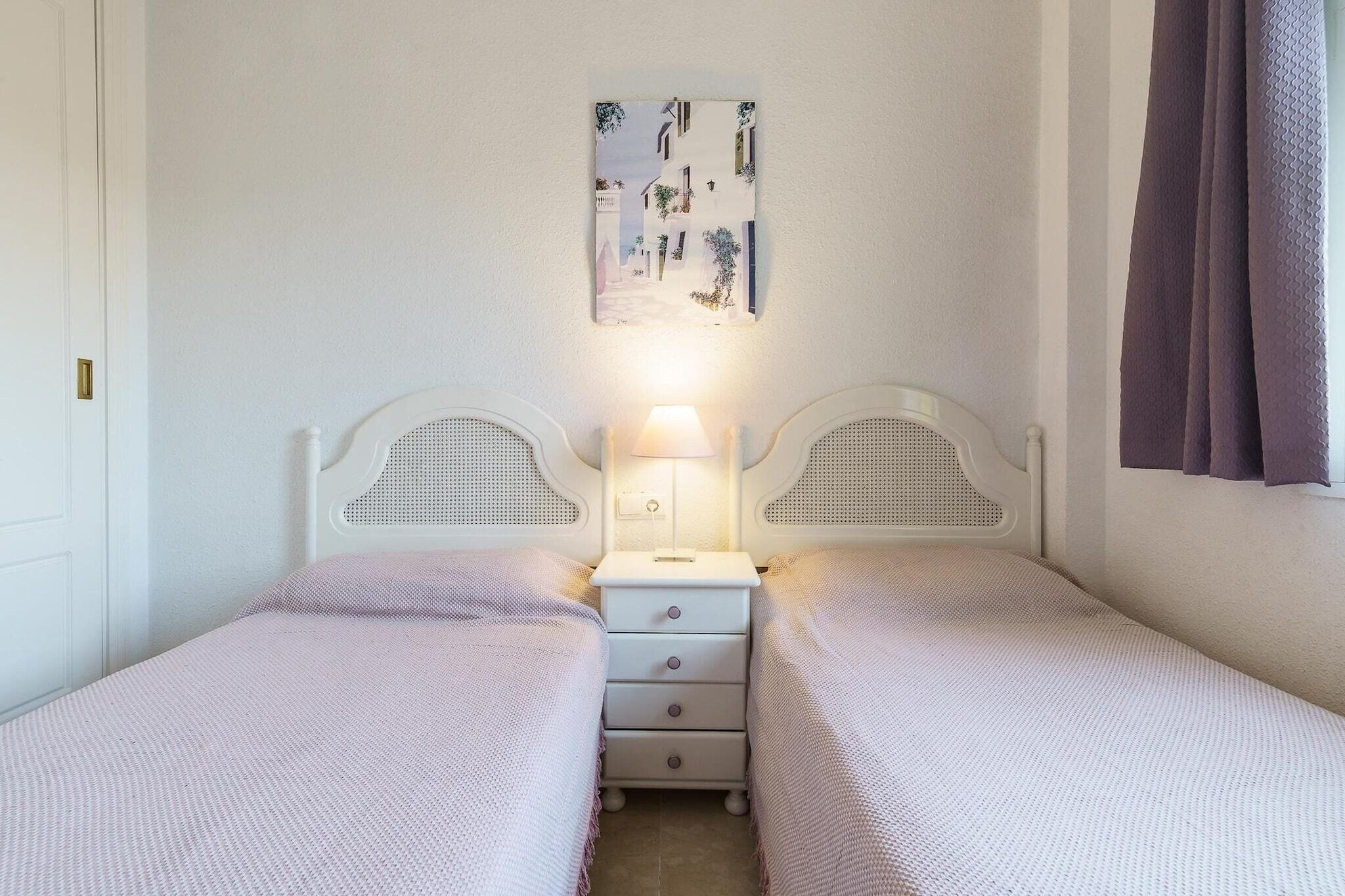 Een slaapkamer met twee eenpersoonsbedden, een nachtkastje met een lamp en een aan de muur hangend schilderij.