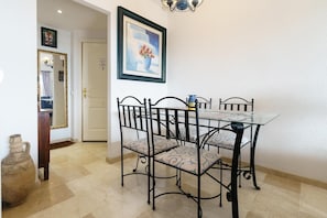 A dining area with a glass table and black metal chairs, a framed painting above the table, and a door leading to another room. - Apartment with communal pool (Mijas)
