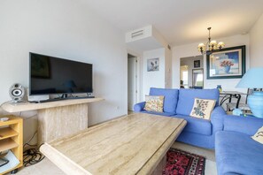 A living room with a flat-screen TV, a blue sofa, a wooden coffee table, and a patterned rug. - Apartment with communal pool (Mijas)