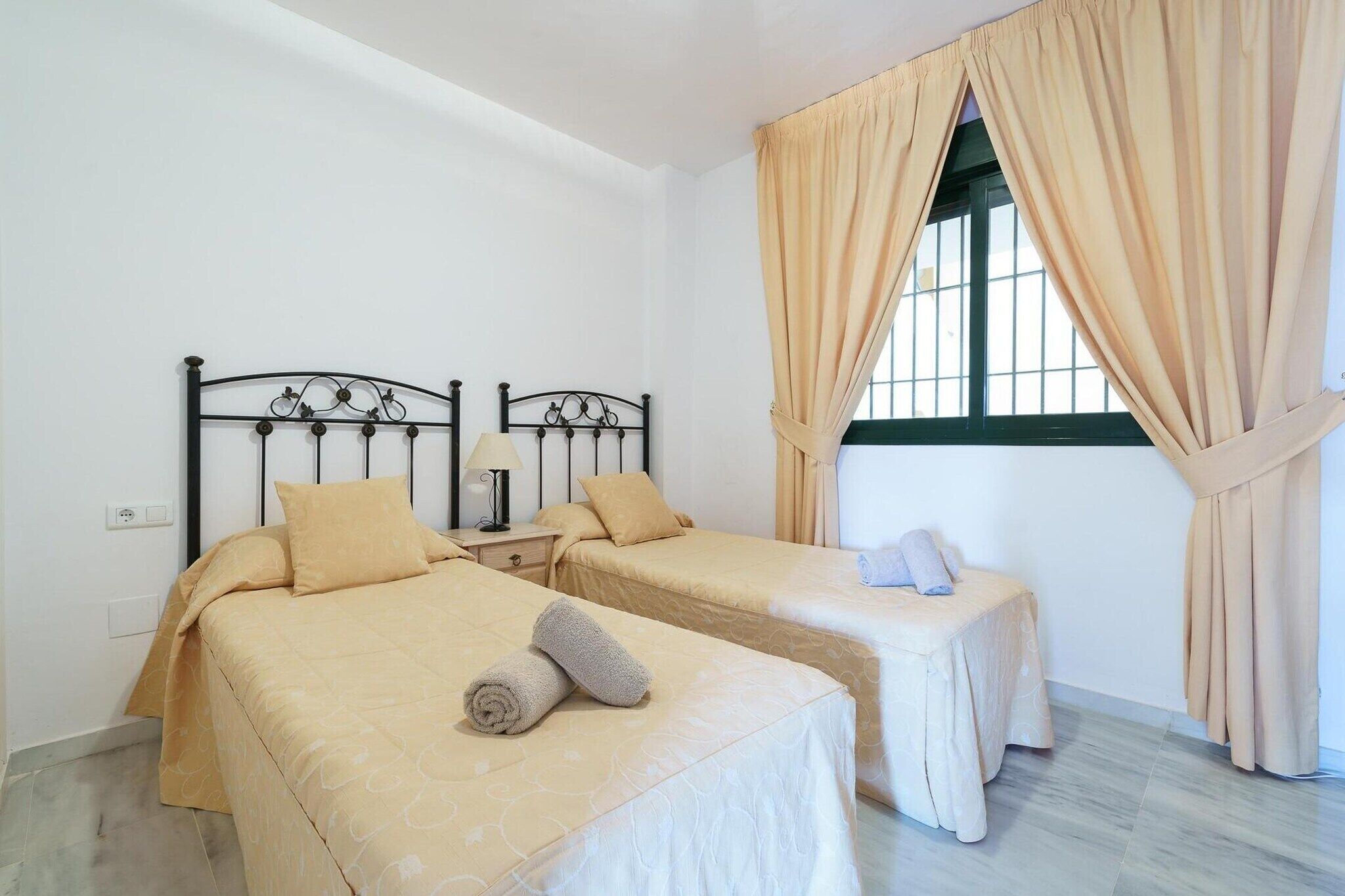 Une chambre avec deux lits, une table de chevet avec une lampe et une fenêtre avec des rideaux.