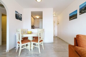 A dining area with a table and chairs, a kitchen visible through an archway, and a living area with a sofa.