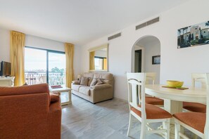 A modern living room with a sofa, a dining table with chairs, and a large window.