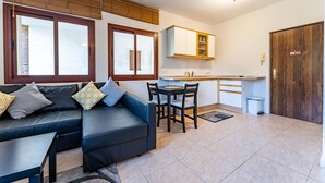 A modern living room with a black sofa, a dining table with chairs, and a kitchen area with cabinets and a countertop. - Apartment in preferred in Cala de Mijas (Mijas)