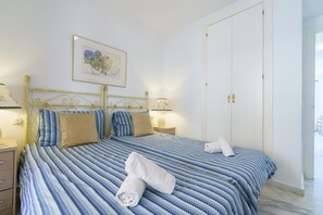 A neatly made bed with a striped blue and white bedspread, two pillows, and two rolled towels on the bed. - Apartment in Mijas with pool (Mijas)