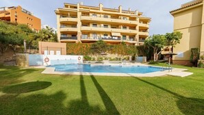 A swimming pool surrounded by well-maintained grass, with a multi-story building in the background. - Apartment in Mijas with pool (Mijas)