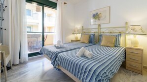 A bedroom with a bed, two bedside tables, a window with curtains, a chair, and a framed picture on the wall. - Apartment in Mijas with pool (Mijas)
