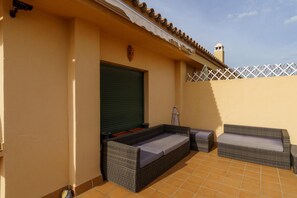 Una terraza con zona de estar techada, un cerrojo cerrado y una valla blanca.