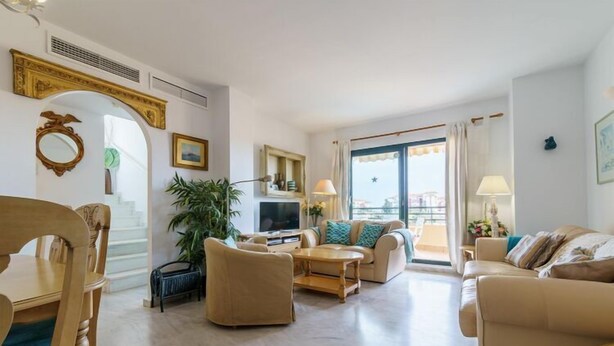 A spacious living room with a sofa set, a coffee table, and a TV. There is a plant, a window with curtains, and a door leading to another room. - Apartment in Mijas with pool (Mijas)