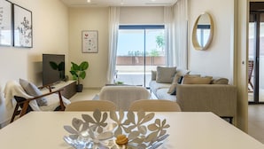 Un salon moderne comprenant une table à manger, un canapé et un téléviseur. Il y a également un balcon avec vue sur l’extérieur.