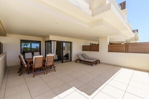 A covered patio with a dining table and chairs, a sun lounger, and a glass door leading to an interior space. - Modern apartment in Mijas Costa (Mijas)