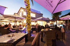 An outdoor dining area with wicker furniture and umbrellas, a bar in the background, and a sign for 'OLIVIAE CHAMPAGNE'. - Modern apartment in Mijas Costa (Mijas)