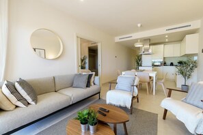 A modern living room with a sofa, armchairs, a coffee table with plants, a dining area with chairs, and a kitchen in the background. - Modern apartment in Mijas Costa (Mijas)