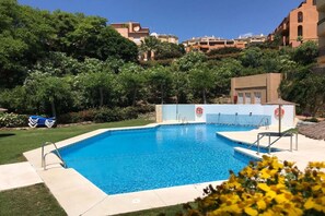 A swimming pool with a lifeguard tower, surrounded by lush greenery and residential buildings in the background.
