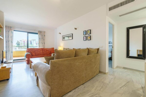 A modern living room with a sofa set, a dining table, and a large window offering a view of buildings outside.