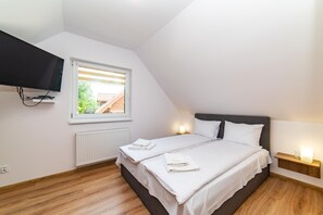 Une chambre à coucher comprenant un lit, un téléviseur fixé au mur, une fenêtre avec des stores et une table de chevet avec une lampe.