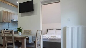 A compact room with a bed, a dining table with chairs, a potted plant, and a TV mounted on the wall. - Comfortable, convenient apartment, pool included (Jaroslawiec)