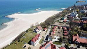 An aerial view of a coastal area with a beach, residential buildings, and a pier. - Spacious 3-room apartment, summer pool (Jaroslawiec)