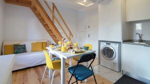 En kompakt opholdsstue med spiseplads, sofa, vaskemaskine og køkken.