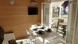 Un interior de madera con una mesa de comedor preparada para cuatro personas, sillas blancas y un televisor montado en la pared.