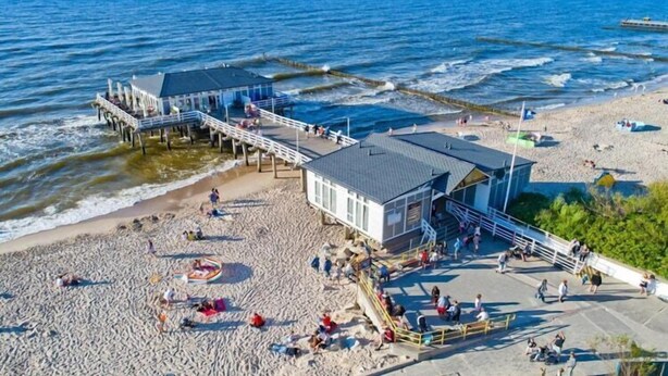 Un muelle frente a la playa con una caseta de salvavidas y una zona de estar techada.