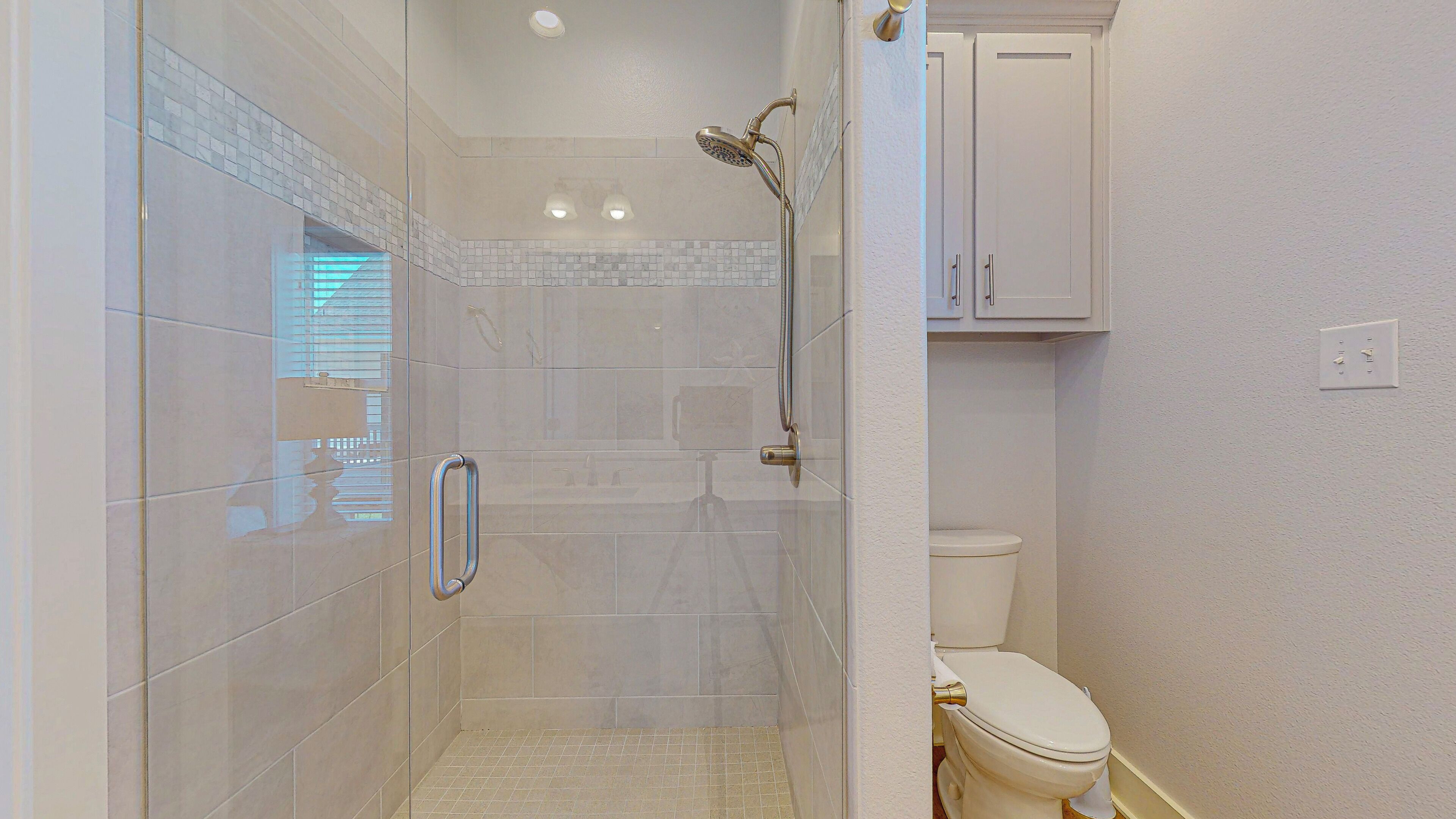 A bathroom with a glass shower enclosure, a toilet, and a cabinet.