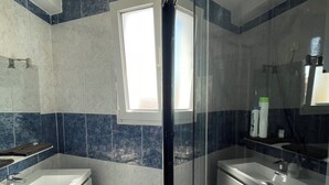 Un bagno moderno con cabina doccia in vetro, una grande finestra e un mobile lavabo con specchio.