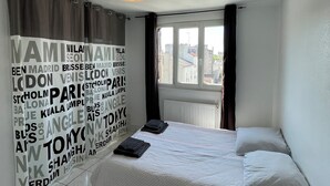 Una camera da letto con un letto, una finestra con tende, un muro con nomi di città e una luce a soffitto.